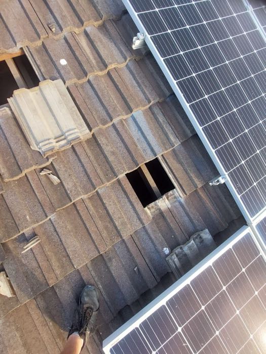 Tile roof with broken and missing tiles beside a solar array
